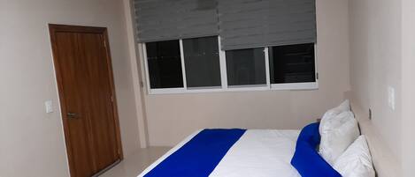 A bedroom with a bed, a window with blinds, a ceiling fan, and a door.