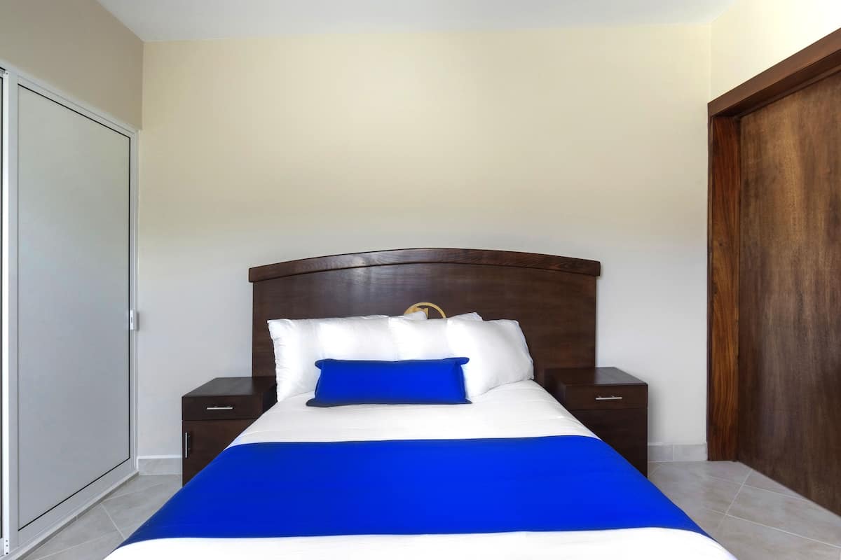 Un dormitorio con una cama, cabecera de madera, dos mesitas de noche y un armario.