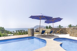 Un área de piscina con dos piscinas, sillones reclinables y sombrillas.