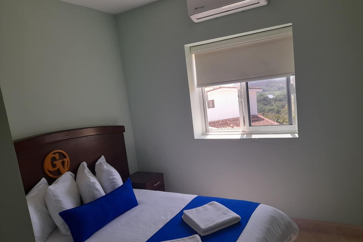 Habitación de hotel con cama, mesita de noche, ventana con vistas y unidad de aire acondicionado.