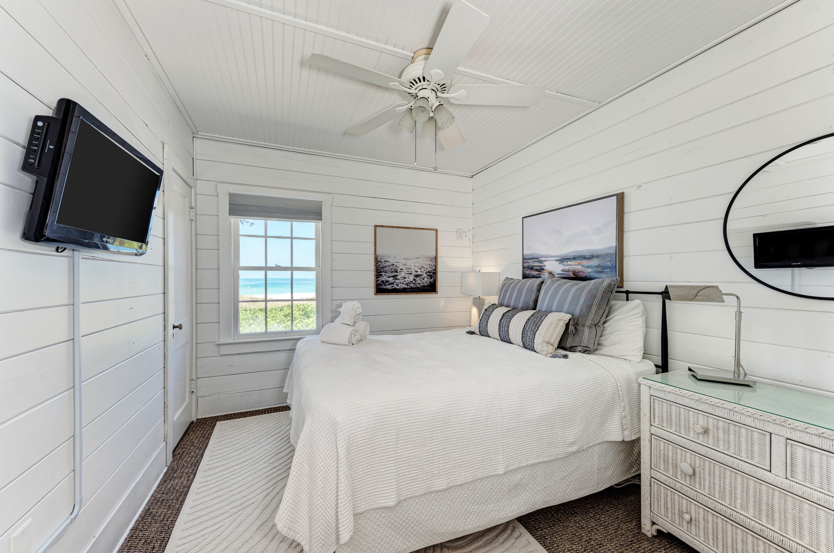 Une chambre à coucher comprenant un lit, une télévision, un ventilateur de plafond, une fenêtre avec vue et une commode.