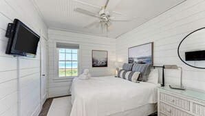Un dormitorio con cama, televisión, ventilador de techo, ventana con vistas y cómoda.