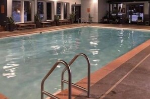 An indoor swimming pool with a metal ladder, surrounded by lounge chairs and a bar area.