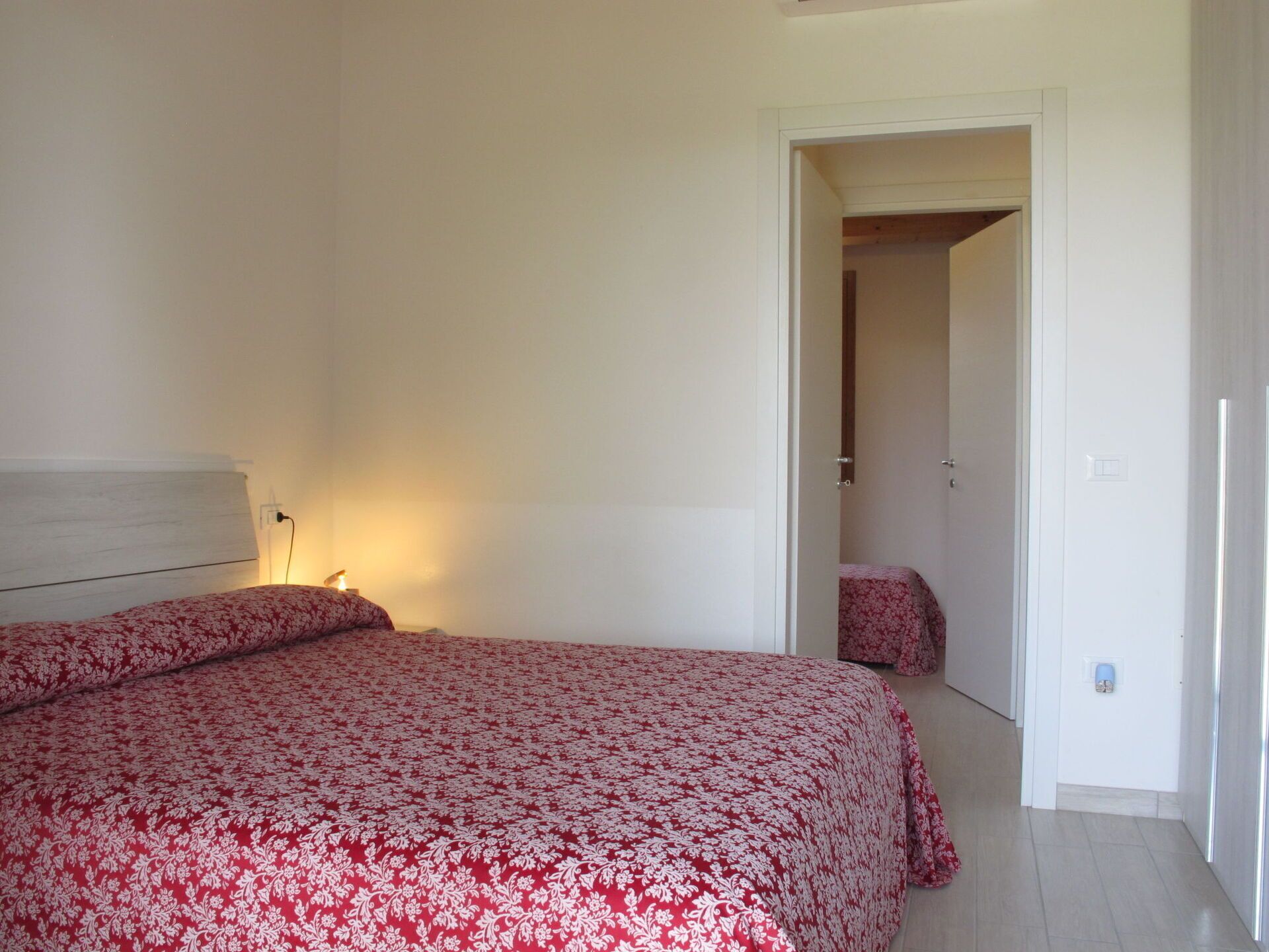 A bedroom with a bed, a bedside lamp, and a door leading to another room.