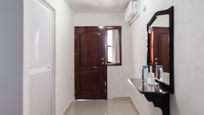 A hallway with a wooden door, a white wall, a black shelf with toiletries, and a ceiling light. - Hotel Casa Poblana (Bacalar)