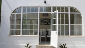A white building with a large arched window, a door, and a small outdoor seating area with chairs. - Villa Maria I (Alvor)
