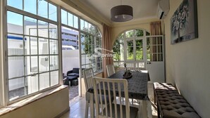 A dining area with a table and chairs, large windows, and a bench. - Villa Maria I (Alvor)