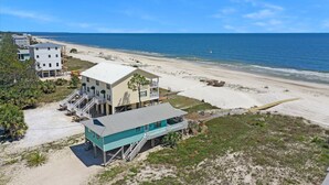 Eine Küstenimmobilie mit mehreren Gebäuden, darunter ein markantes türkisfarbenes Haus mit Balkon, direkt an einem Sandstrand mit Blick auf den Ozean.