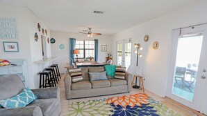 Ein geräumiges Wohnzimmer mit grauem Sofa, einem Essbereich mit Tisch und Stühlen sowie einem großen Fenster mit Vorhängen.