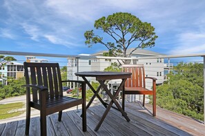 A wooden deck with two chairs and a table, overlooking a residential area with houses and a large tree.