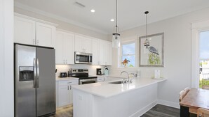 A modern kitchen with white cabinetry, stainless steel appliances, a central island with a sink, and a dining area with a wooden table and chairs.