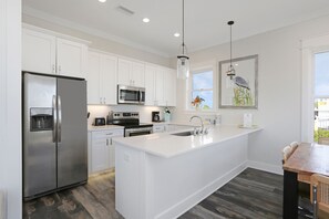 A modern kitchen with white cabinetry, stainless steel appliances, a central island with a sink, and a dining area with a wooden table and chairs. - Old Florida, Near Boat Launch, St Vincent Island, Beach Front ~ Fisherman's Cove (Indian Pass)