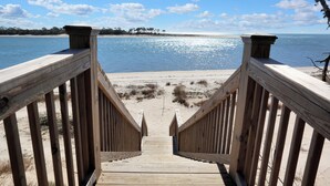 A wooden boardwalk leading to a sandy beach with a clear view of the ocean and a line of trees in the distance.