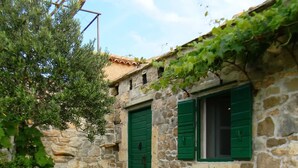 Edificio de piedra con dos puertas verdes y ventanas, rodeado de vegetación y plantas de lavanda.
