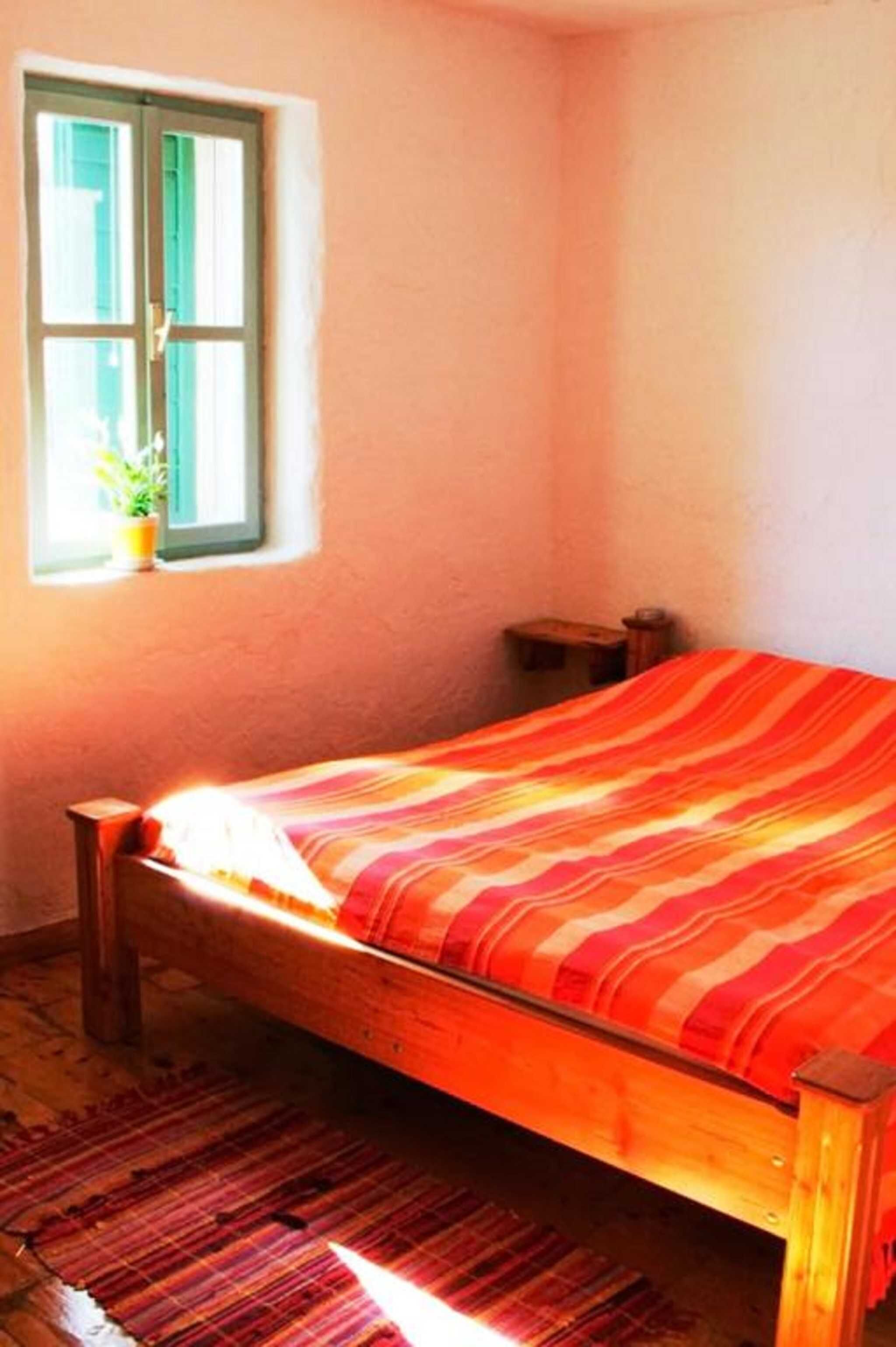 A bedroom with a wooden bed, a window with a view of greenery, and a small bedside table.