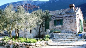 Un edificio de piedra con techo de tejas, una pérgola de madera y una escalera de piedra que conduce a la entrada.
