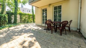 Un patio con mesa y sillas, un área cubierta y vista a un edificio con ventana.