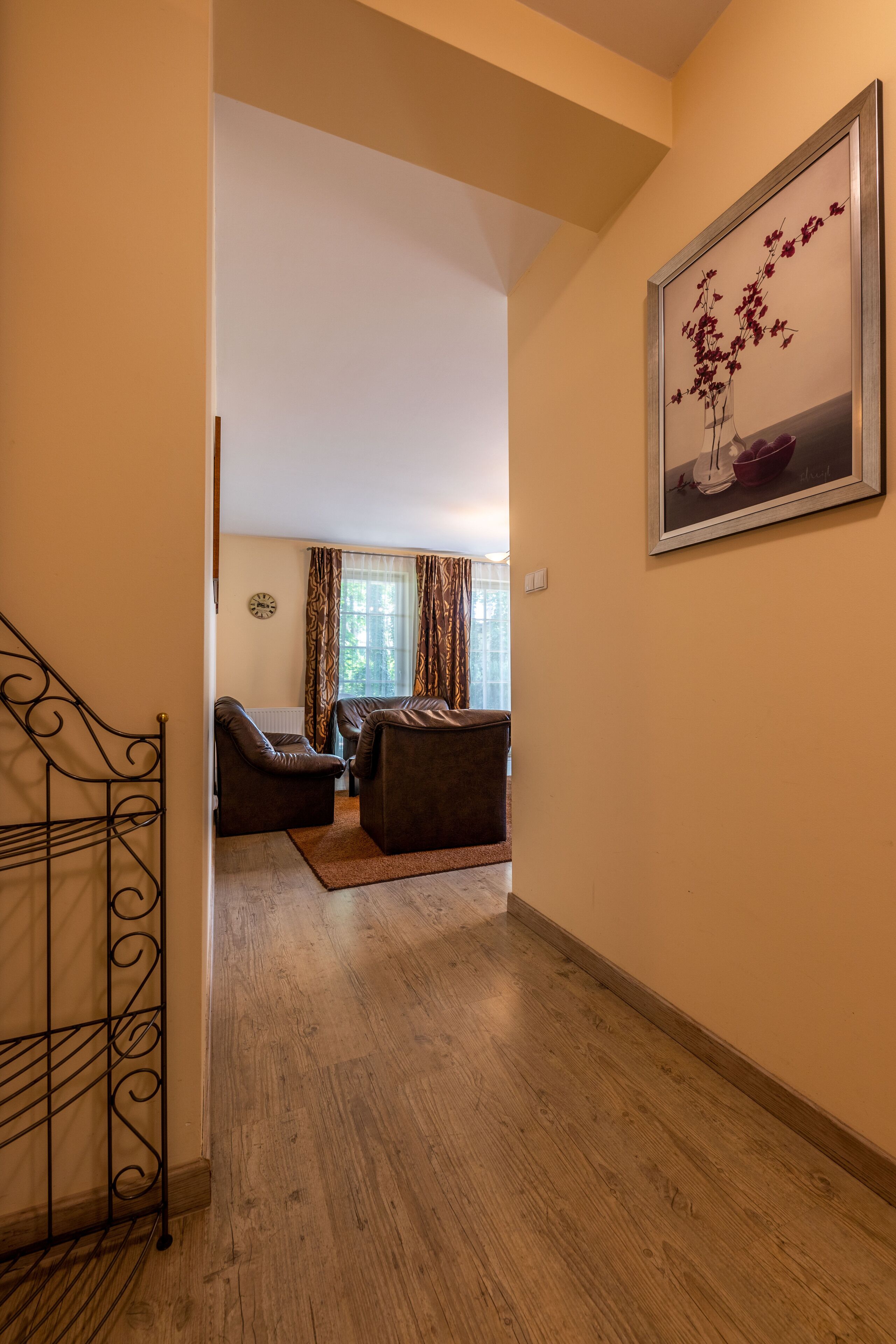 A hallway with a staircase, a living area with two sofas, a rug, and a framed artwork on the wall.