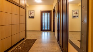 Un pasillo con paneles de madera, una puerta con persianas verticales y dos cuadros en las paredes.