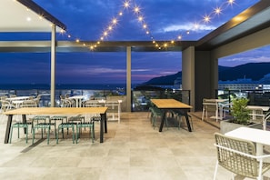 Terraza al aire libre con mesas y sillas, con vistas a un paisaje urbano y al mar.