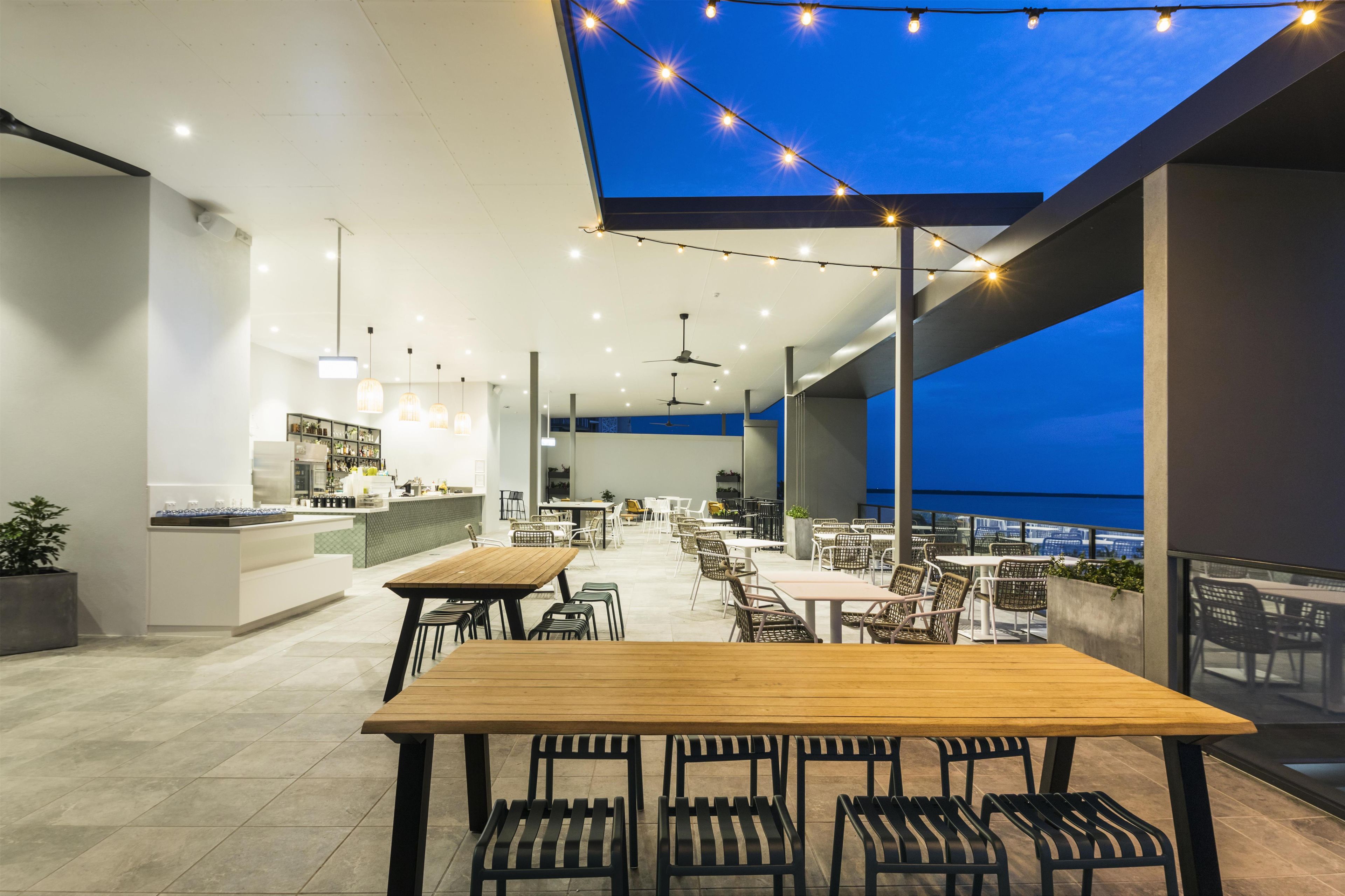 An outdoor dining area with tables and chairs, a bar, and a view of the sea.