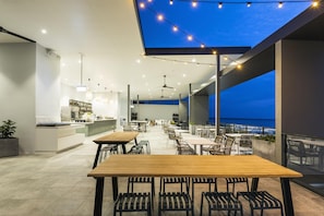 Un área de comedor al aire libre con mesas y sillas, un bar y vista al mar.