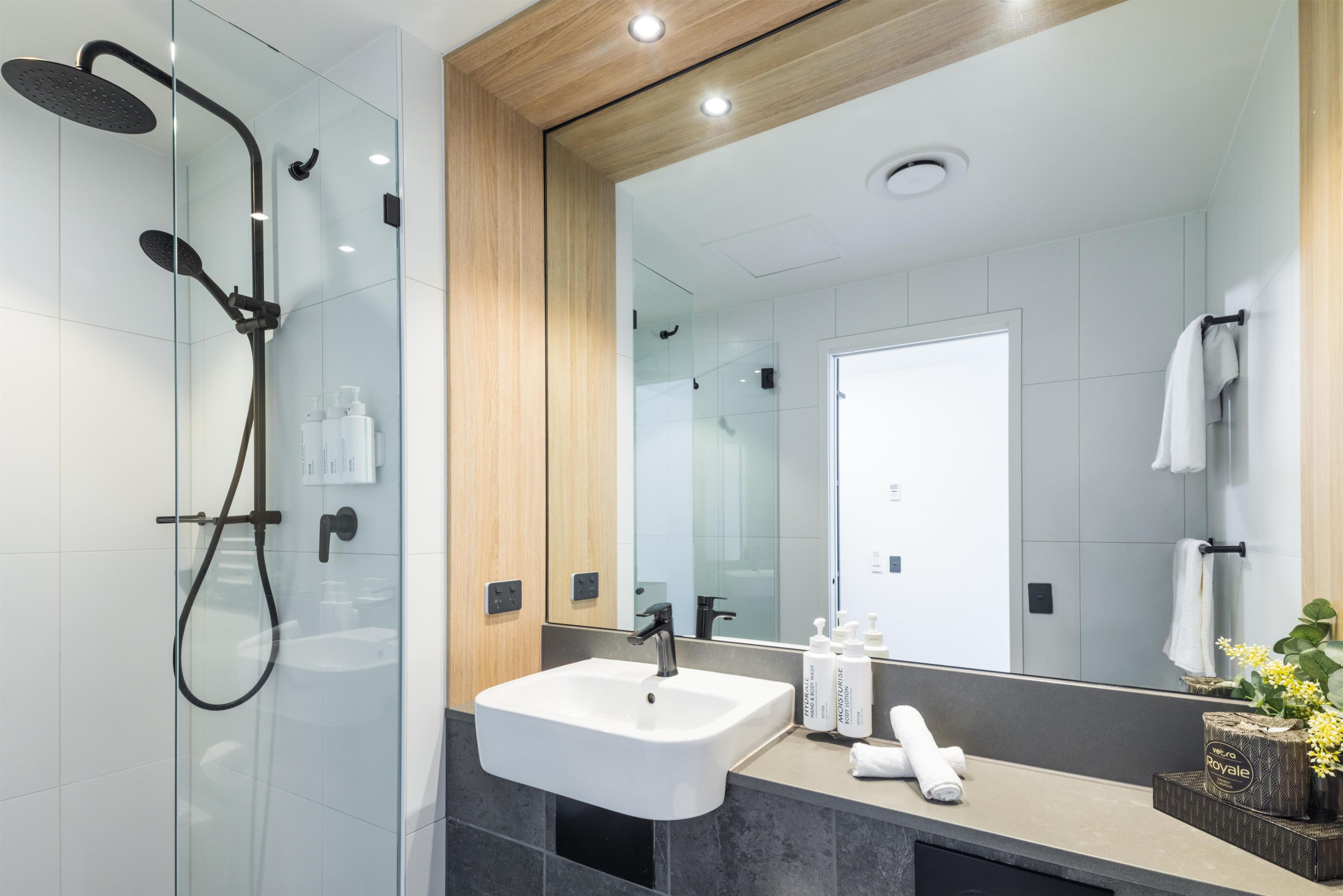 Une salle de bain moderne avec une douche à parois de verre, un lavabo blanc et un grand miroir.