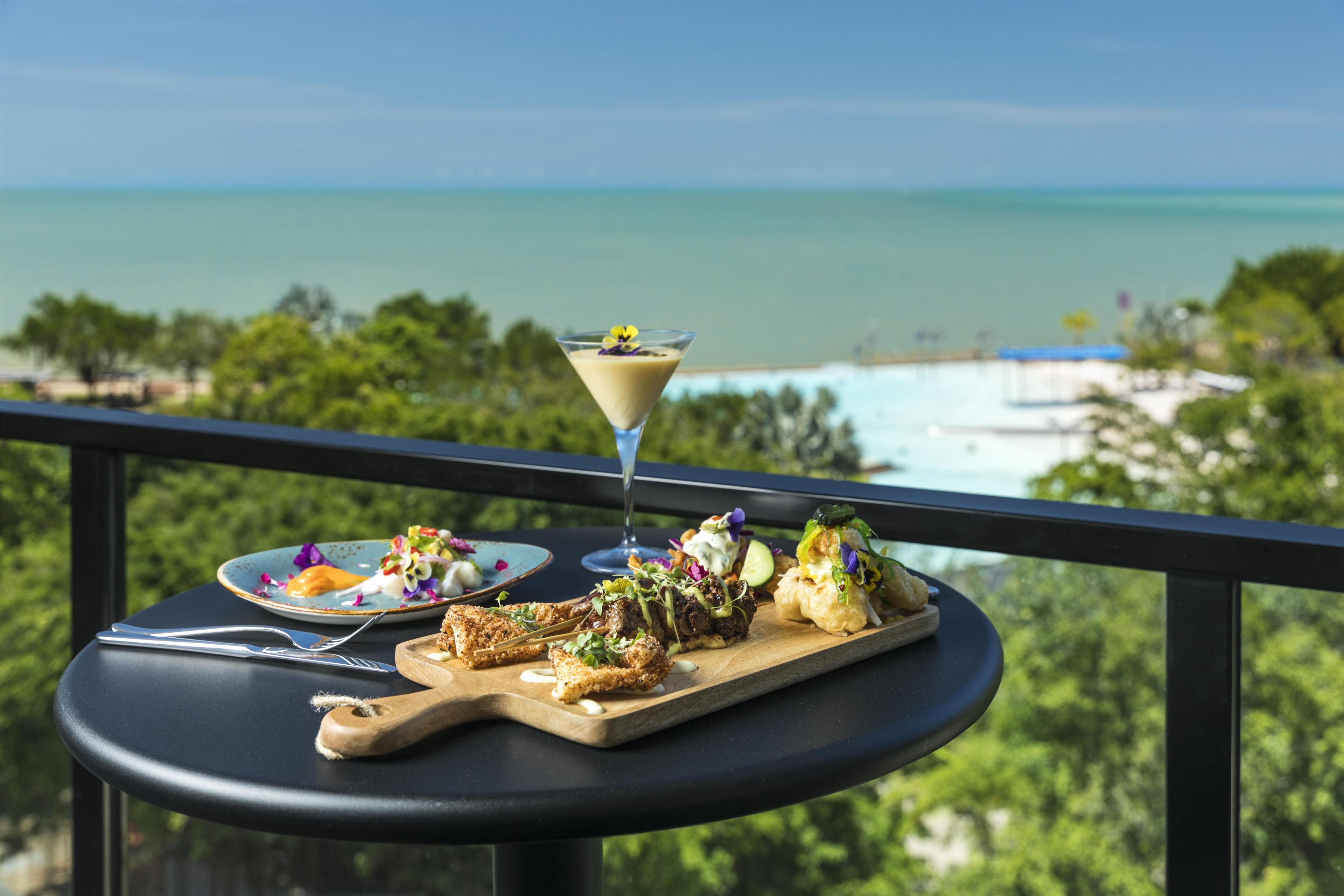 A table with food and a drink on a balcony overlooking a beach.