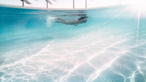 A person swimming in a pool with a clear view of the pool's bottom and a sandy bottom. - Oaks Cairns Hotel (Cairns)