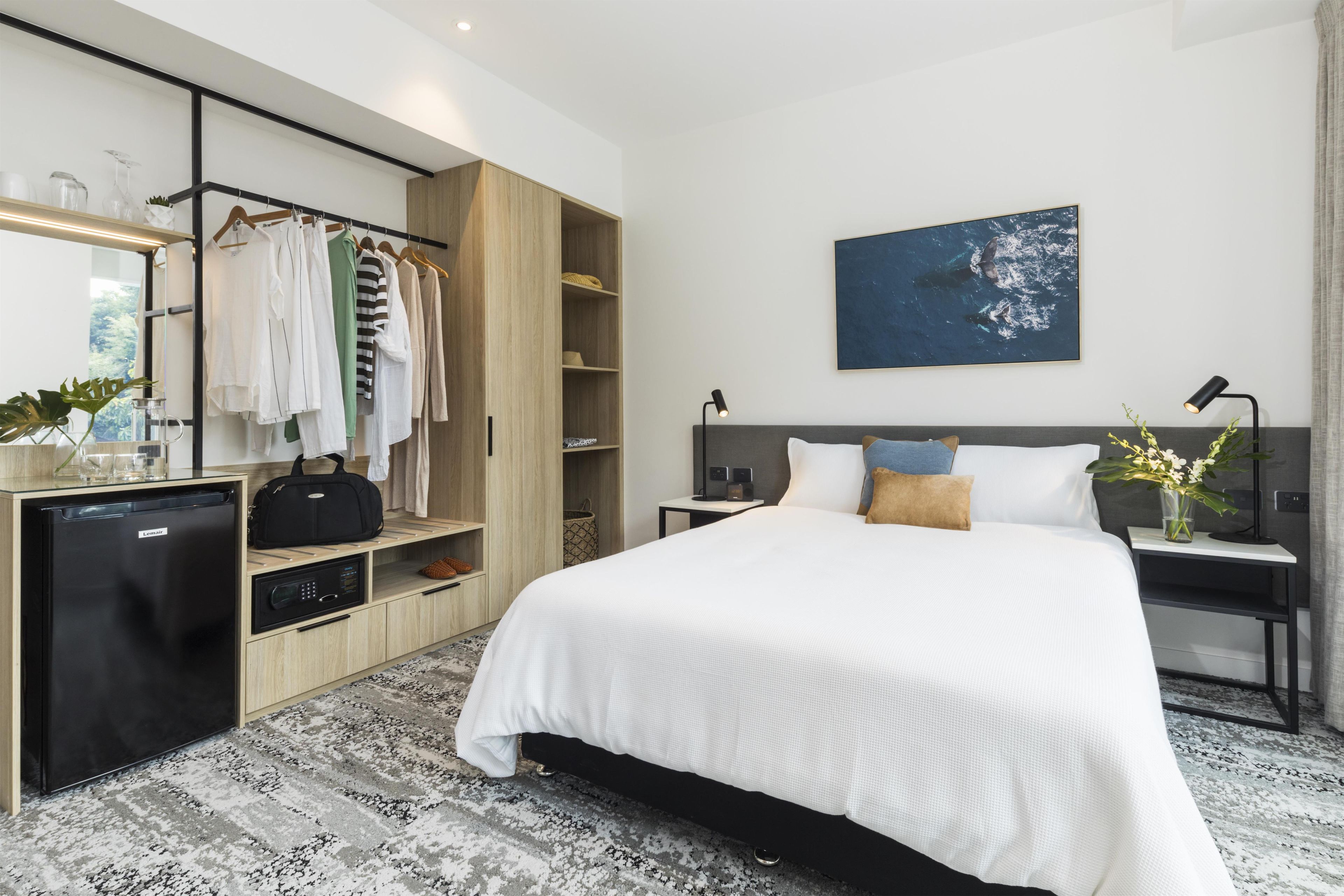 A modern hotel room with a bed, bedside table, lamp, and a large window.