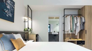 Un dormitorio moderno con una cama grande, mesita de noche y un armario con ropa colgada.