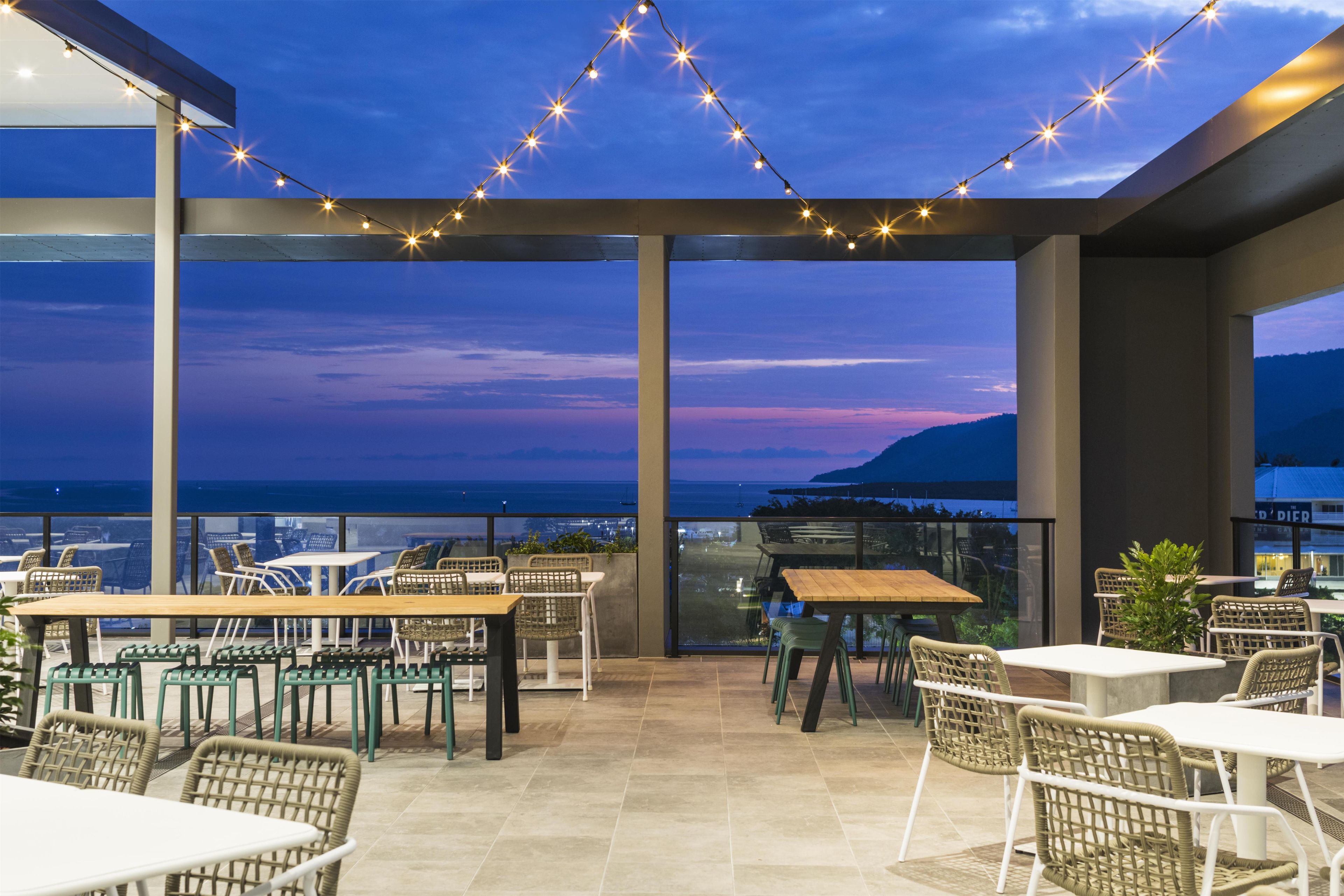 An outdoor patio area with tables and chairs, string lights, and a view of the ocean.