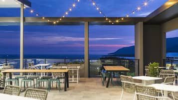An outdoor patio area with tables and chairs, string lights, and a view of the ocean.