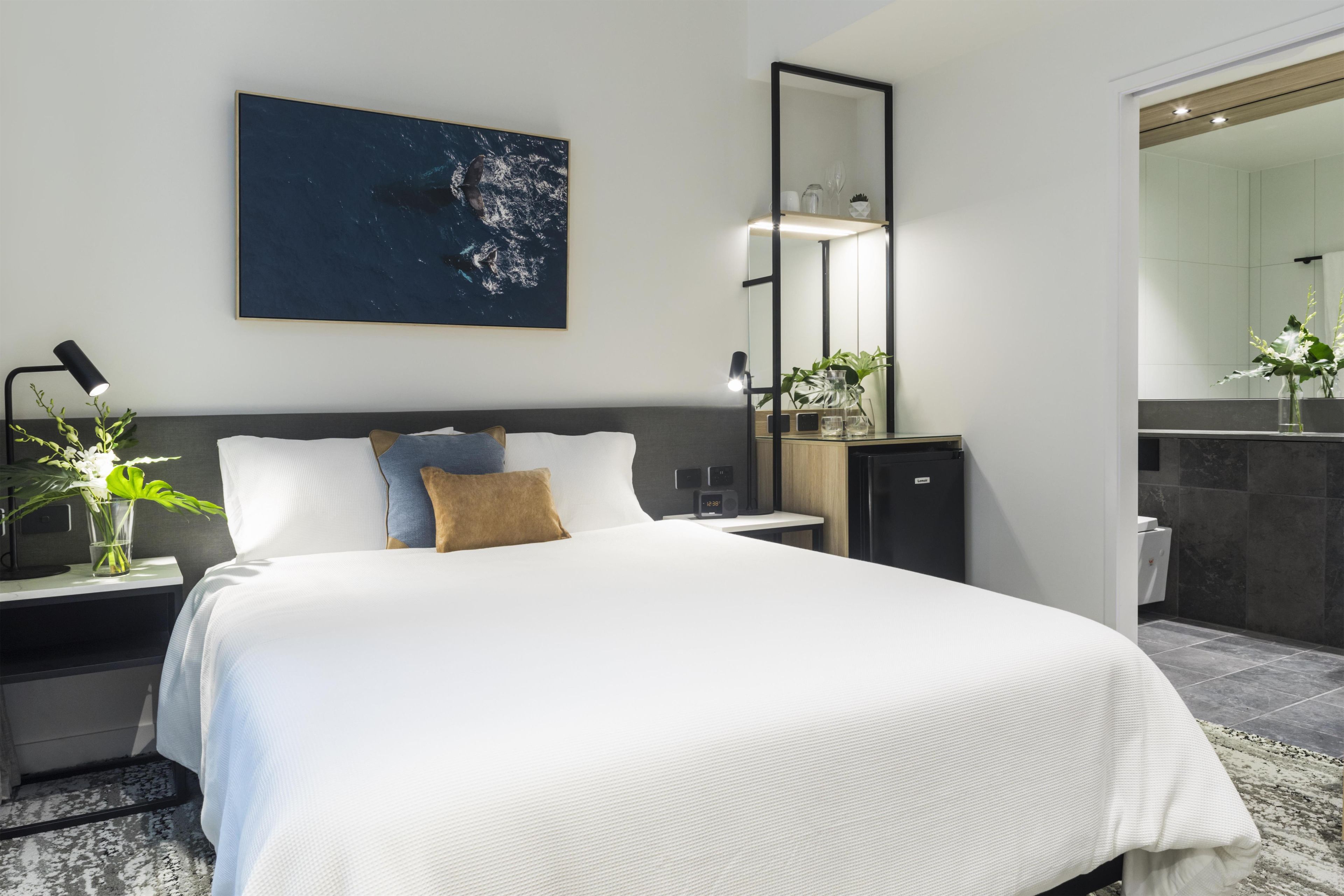 A modern hotel room with a large bed, bedside tables, a nightstand, a mirror, and a view of the bathroom.