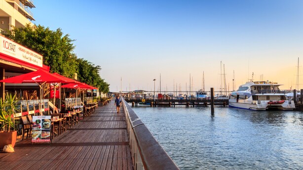 Un muelle de madera con mesas al aire libre y vista al puerto deportivo.