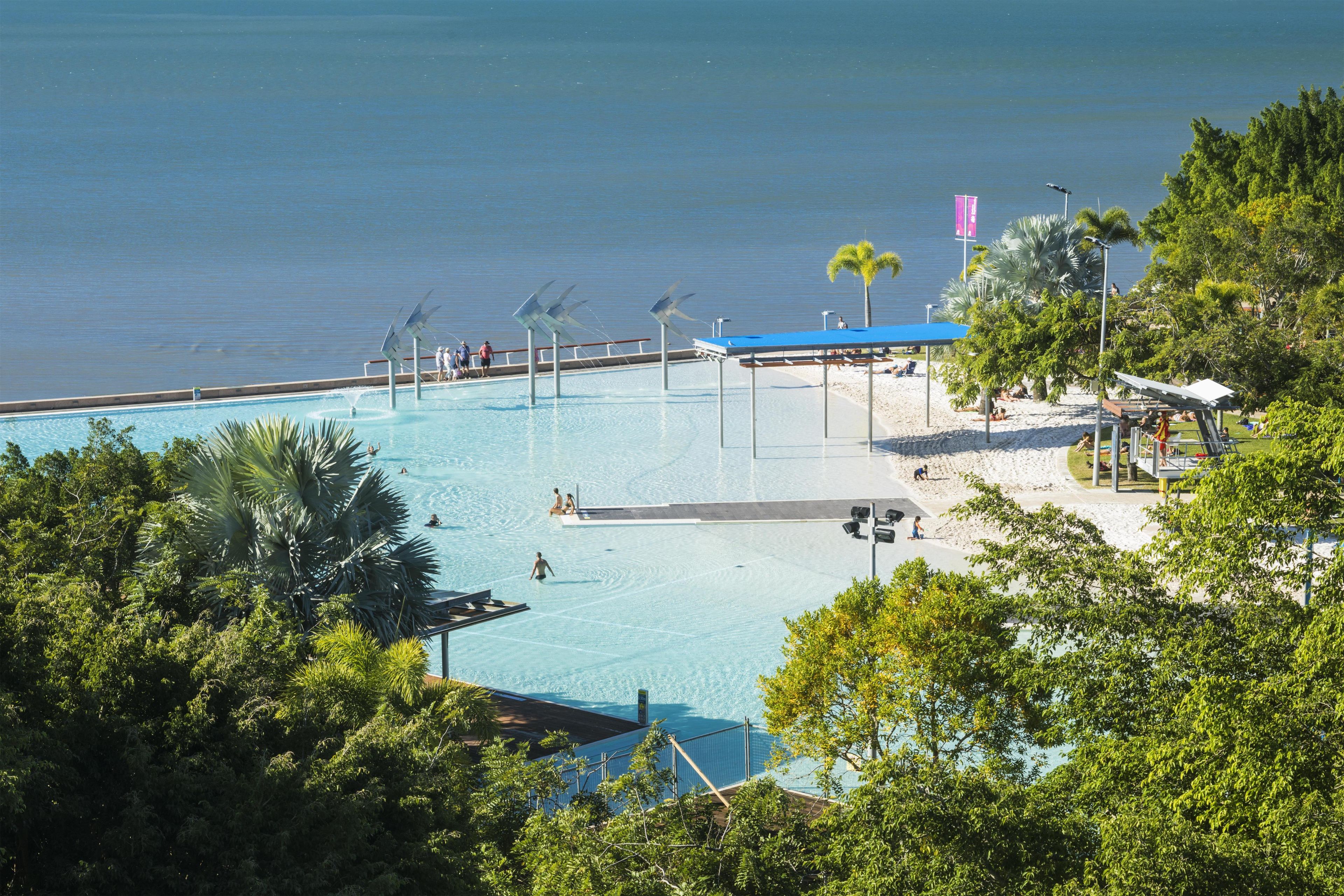 A pool area with a view of the sea, surrounded by trees and a beach.