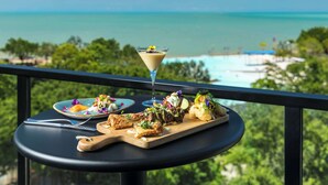 Una mesa de comedor con varios platos y una copa de martini, con vistas panorámicas al océano.