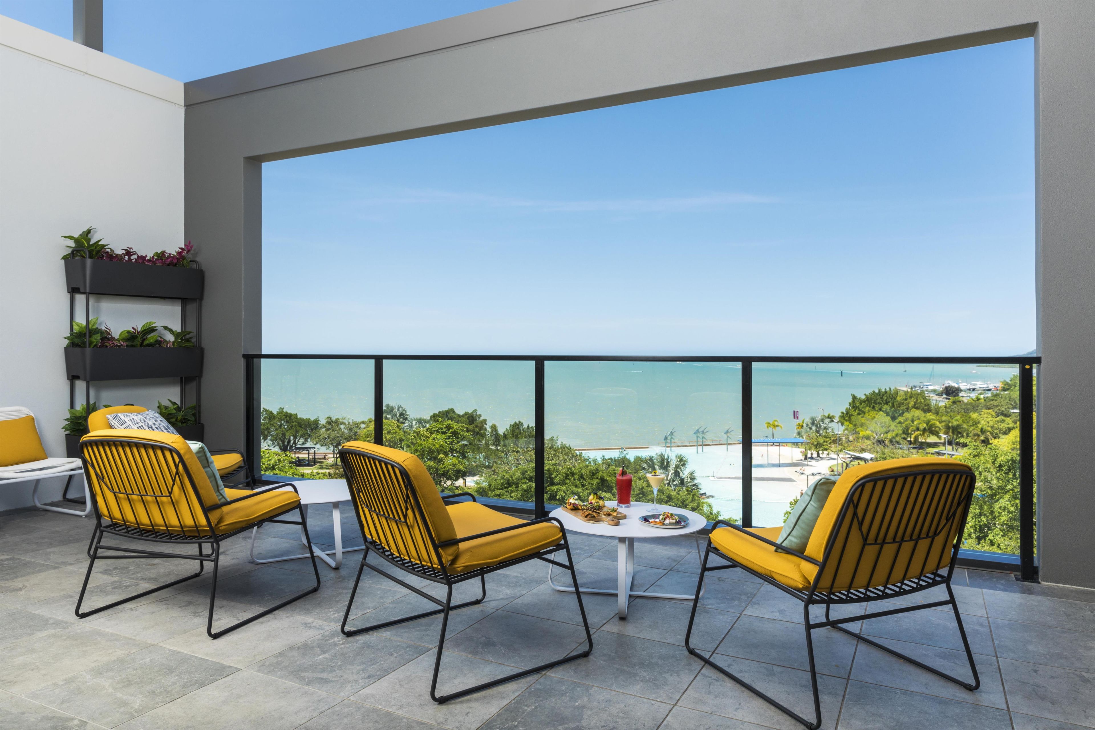 A balcony with yellow chairs, a small table, and a view of the sea.