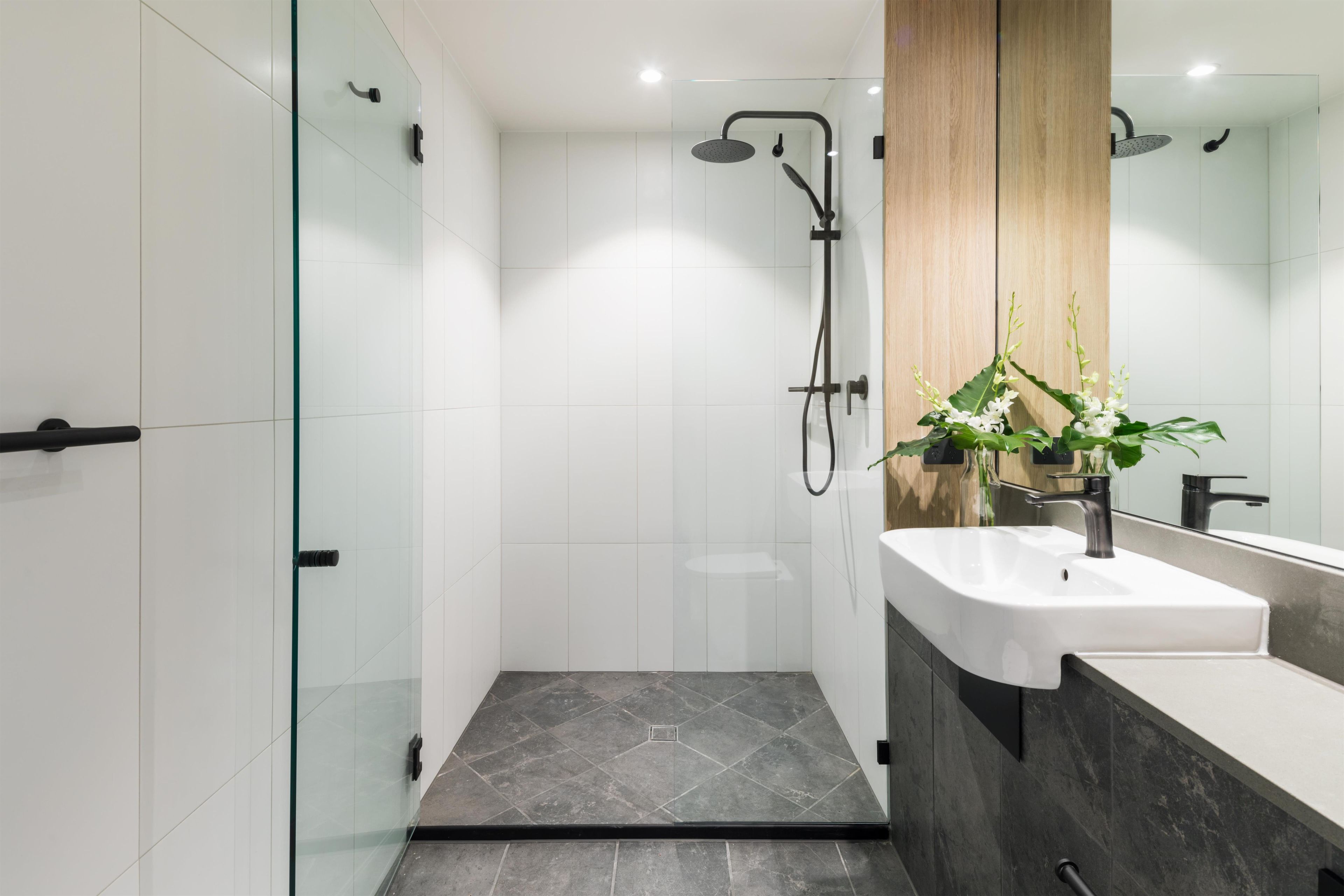 A modern bathroom with a glass shower enclosure, a white sink, and a wooden vanity.