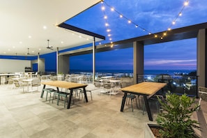 An outdoor dining area with tables and chairs, string lights, and a view of the cityscape at dusk. - Oaks Cairns Hotel (Cairns)