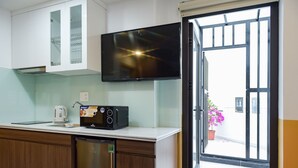 A modern kitchen with a built-in microwave, a kettle, and a dishwasher. A flat-screen TV is mounted above the counter, and a sliding glass door leads to an outdoor area with a potted plant. - Rainbow Apartment Hai Phong (Hai Phong)