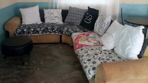 A corner living room with a sofa, a small round table, and a window with curtains. - Firebird Inn (Naivasha)