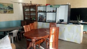 A dining area with a wooden table and chairs, a kitchen area with a refrigerator and stove, and a dining table with a white tablecloth. - Firebird Inn (Naivasha)
