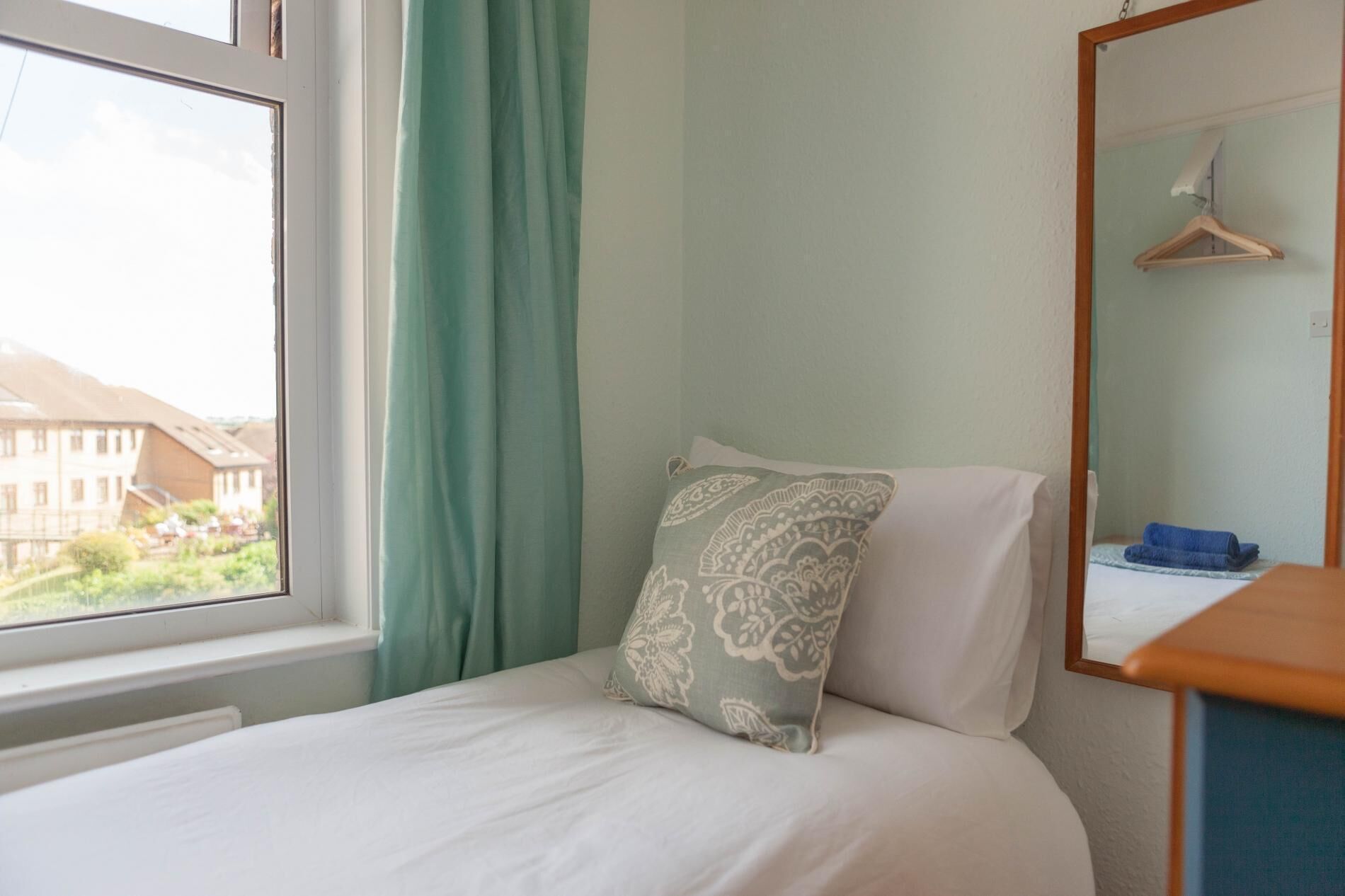 A bedroom with a bed, a window with curtains, a bedside table, and a mirror.