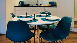 A modern kitchen with white cabinets, a built-in oven, and a dining area with a round table and teal chairs.