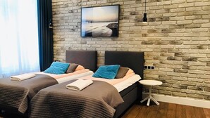 A double bed with two pillows, a bedside table, and a wall-mounted TV in a room with a brick wall and wooden flooring.
