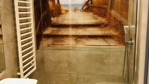 A bathroom with a shower, toilet, and a glass partition with a beach scene.