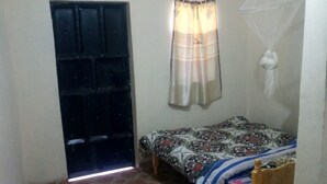 A small, dimly lit room with a single bed, a wooden table, and a window with a curtain.