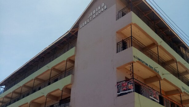 A multi-story building with balconies and signs for 'JERIKO GUEST HOUSE' and 'LEUM-G FURNITURE & ELECTRONICS'.