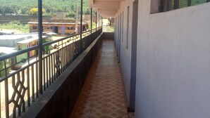 A corridor with a tiled floor, a railing, and a view of buildings and greenery outside.